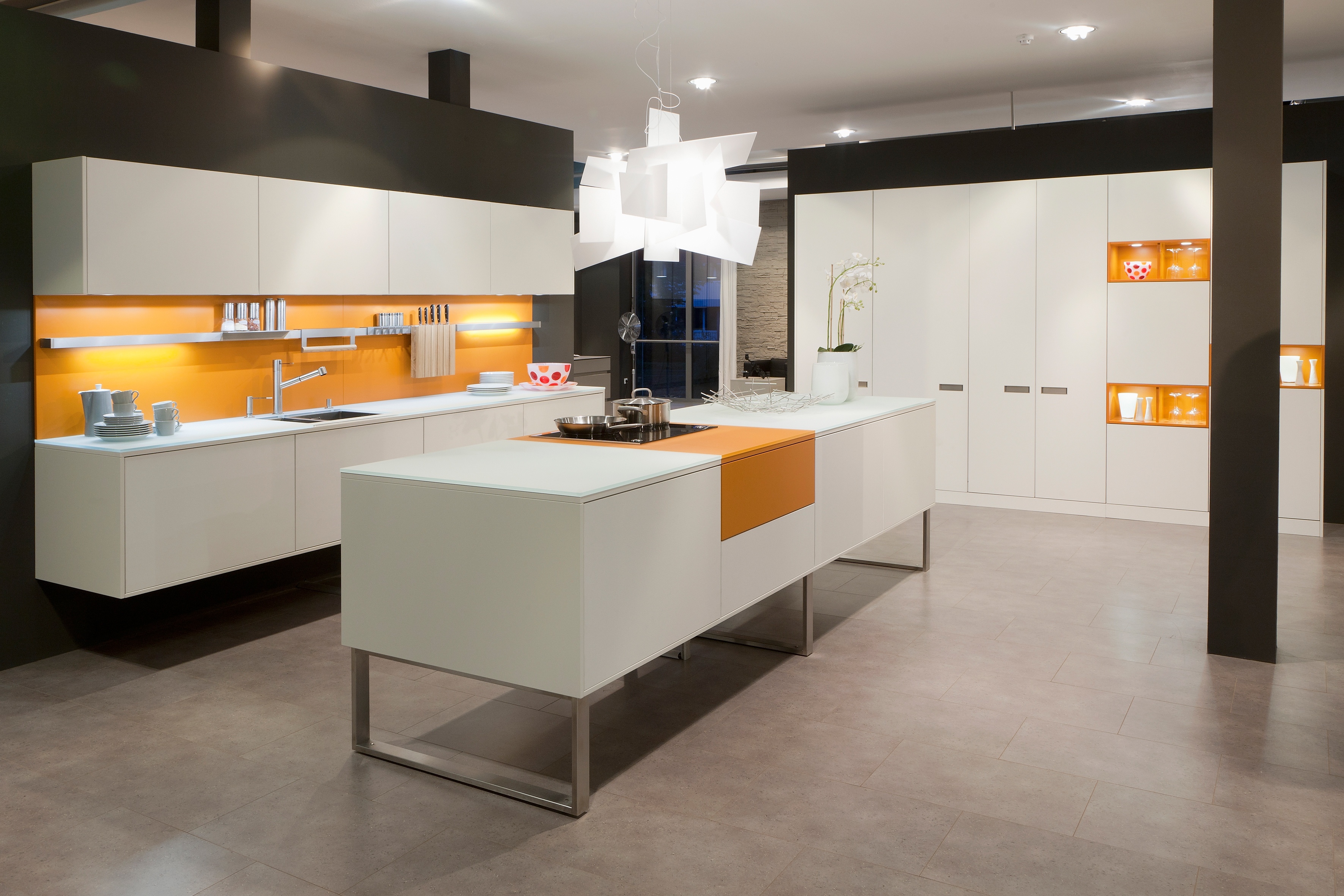 Ballerina Küche in weiß mit orangenene Akzenten. Kücheninsel auf einem Kufengestell, schwebende Unterschrankzeile und Hochschränke.