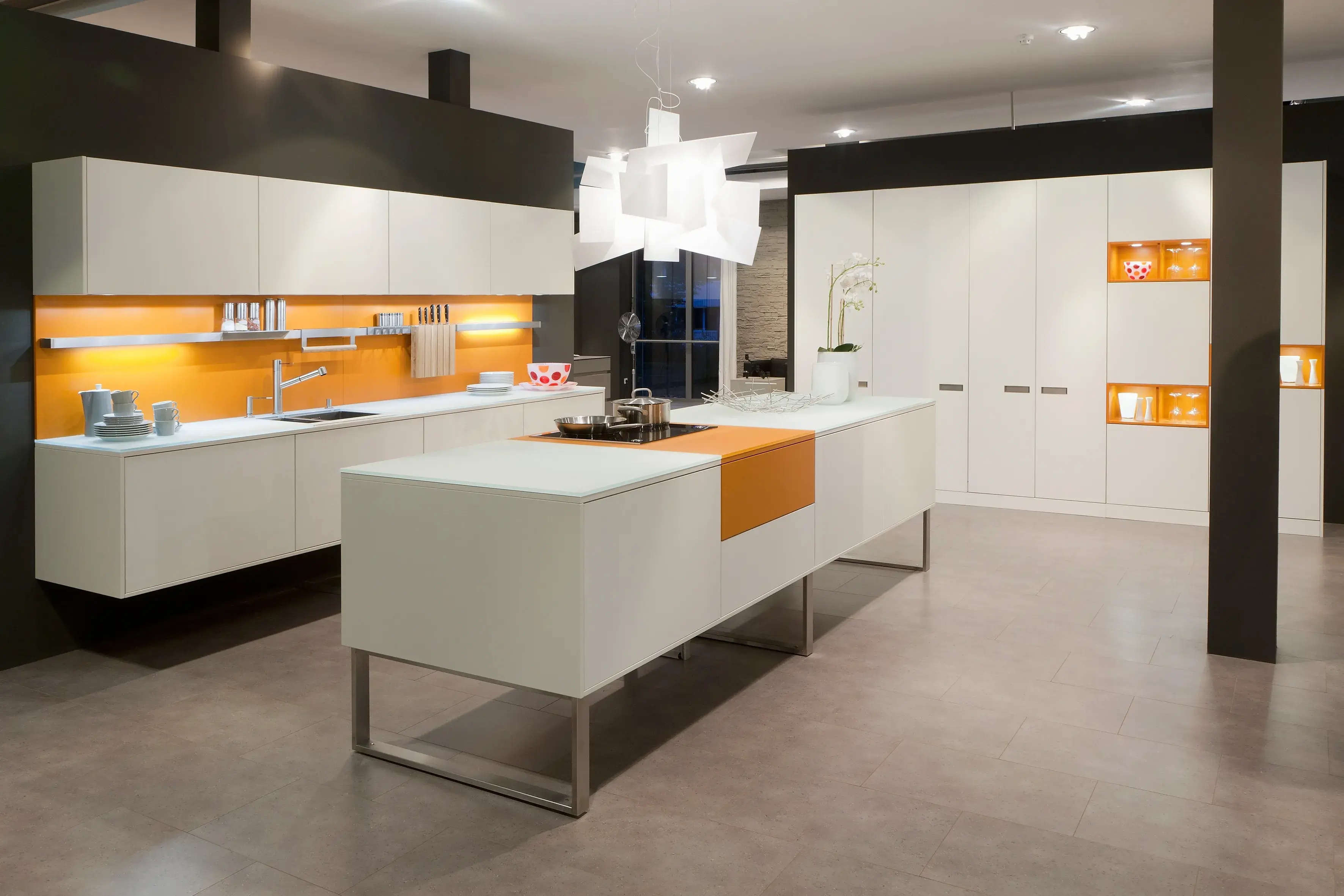 Ballerina Küche in weiß mit orangenene Akzenten. Kücheninsel auf einem Kufengestell, schwebende Unterschrankzeile und Hochschränke.